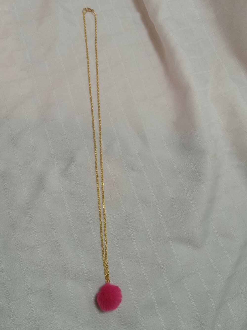 Handmade necklace with a small pom-pom and gold-colored accent hooks and chains